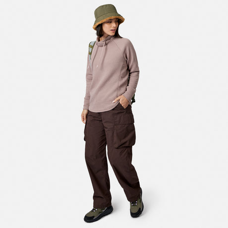 Person wearing a textured mauve Women’s UltraFill Cowl Neck Top, dark brown cargo pants, an olive green bucket hat, and hiking sneakers.