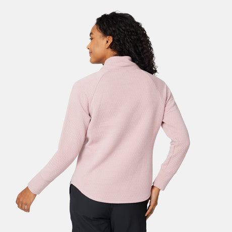 A woman with curly hair, seen from behind, wears a light pink Free Country Women's UltraFill Cowl Neck Top with seamless quilting and black pants, standing against a plain white background.