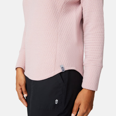 A person is shown from shoulders to mid-thigh wearing a textured light pink Free Country Women's UltraFill Cowl Neck Top with seamless quilting and black pants, their left hand resting by their side.
