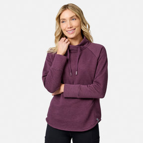 A woman wearing a prune-colored Free Country Women’s UltraFill Cowl Neck Top, featuring seamless quilting, a cowl neck collar, and drawstrings.