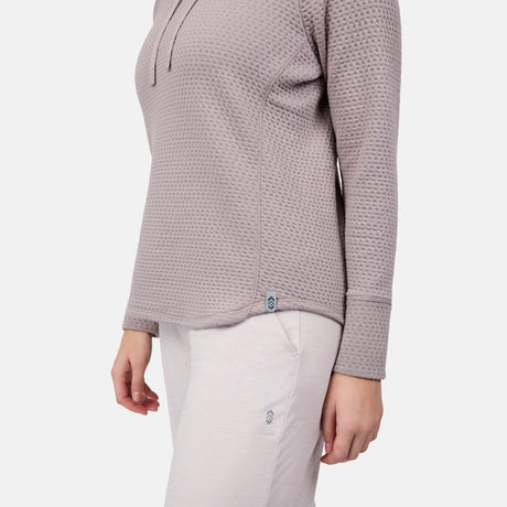 A person wears a textured, light mauve Free Country Women's UltraFill Cowl Neck Top with seamless quilting and light beige pants, shown from shoulders to mid-thigh against a plain white background.