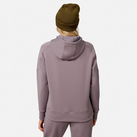 A woman is seen from the back wearing a mauve Free Country Women’s Sueded Lush Pullover Hoodie with matching pants and a brown beanie, standing against a plain white background.