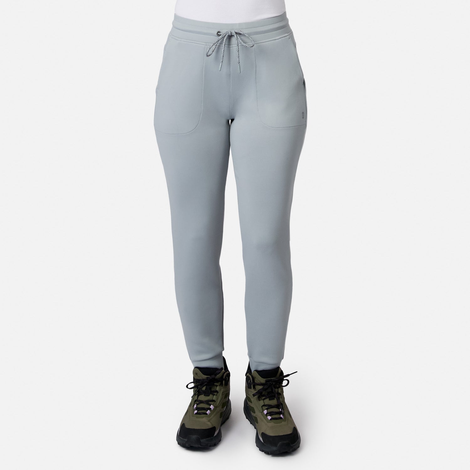A person models the Free Country Women’s Sueded Lush Jogger in light gray, paired with olive green hiking shoes. Only their lower body is shown against a plain white background.