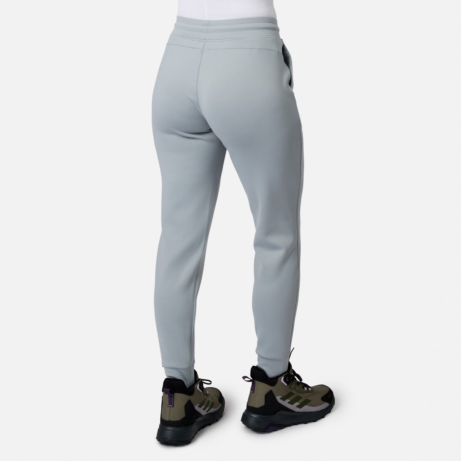 Person wearing Free Country Women’s Sueded Lush Jogger in light gray with black and olive green sneakers, shown from the back against a plain white background.