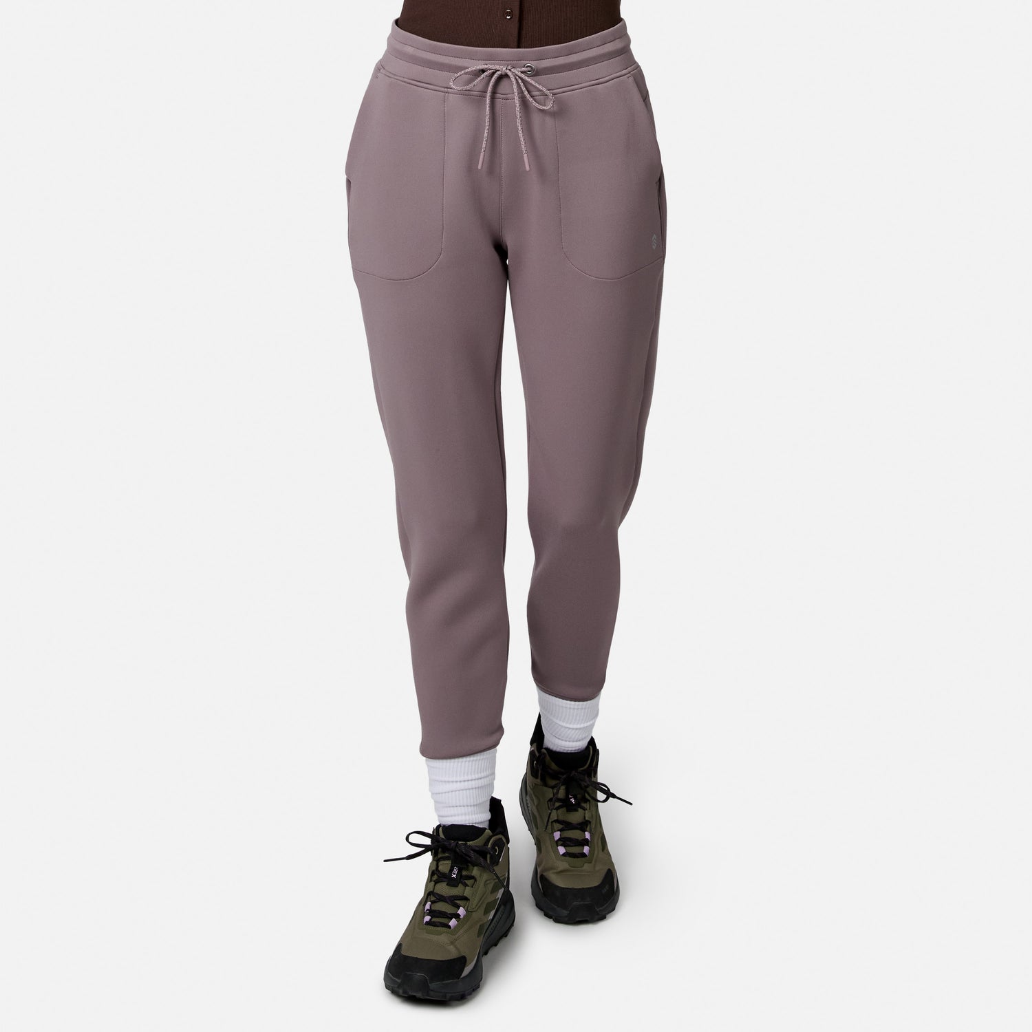 Model in Free Country Women’s Sueded Lush Jogger (mauve, 4-way stretch, front pockets, drawstring waist), white socks, and green hiking shoes on white background. Upper body not visible.