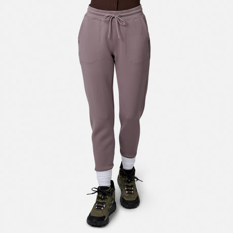 Model in Free Country Women’s Sueded Lush Jogger (mauve, 4-way stretch, front pockets, drawstring waist), white socks, and green hiking shoes on white background. Upper body not visible.