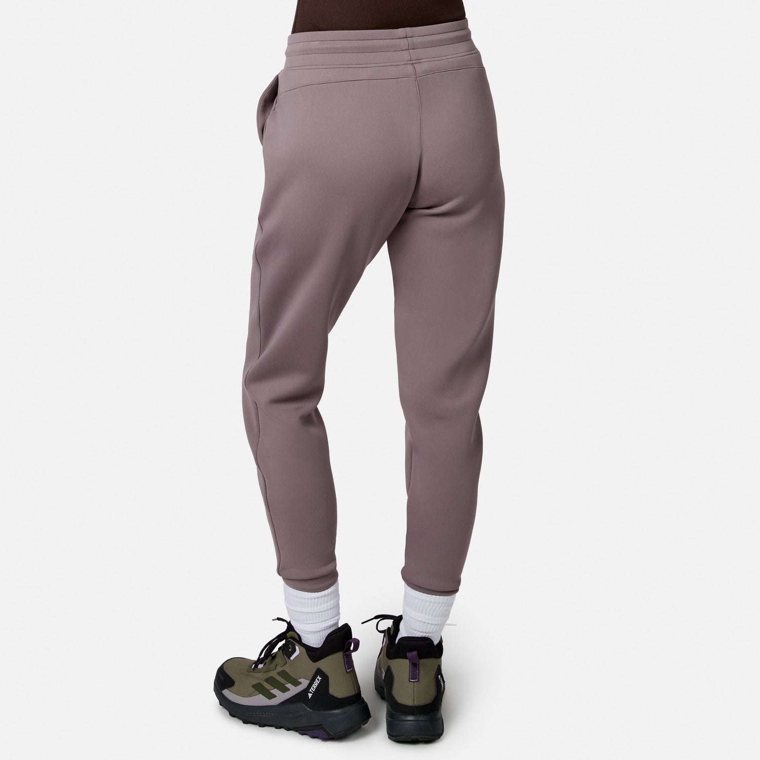 Model wearing Free Country Women’s Sueded Lush Jogger in mauve with white socks and green-black sneakers, shown from the back against a plain white background.