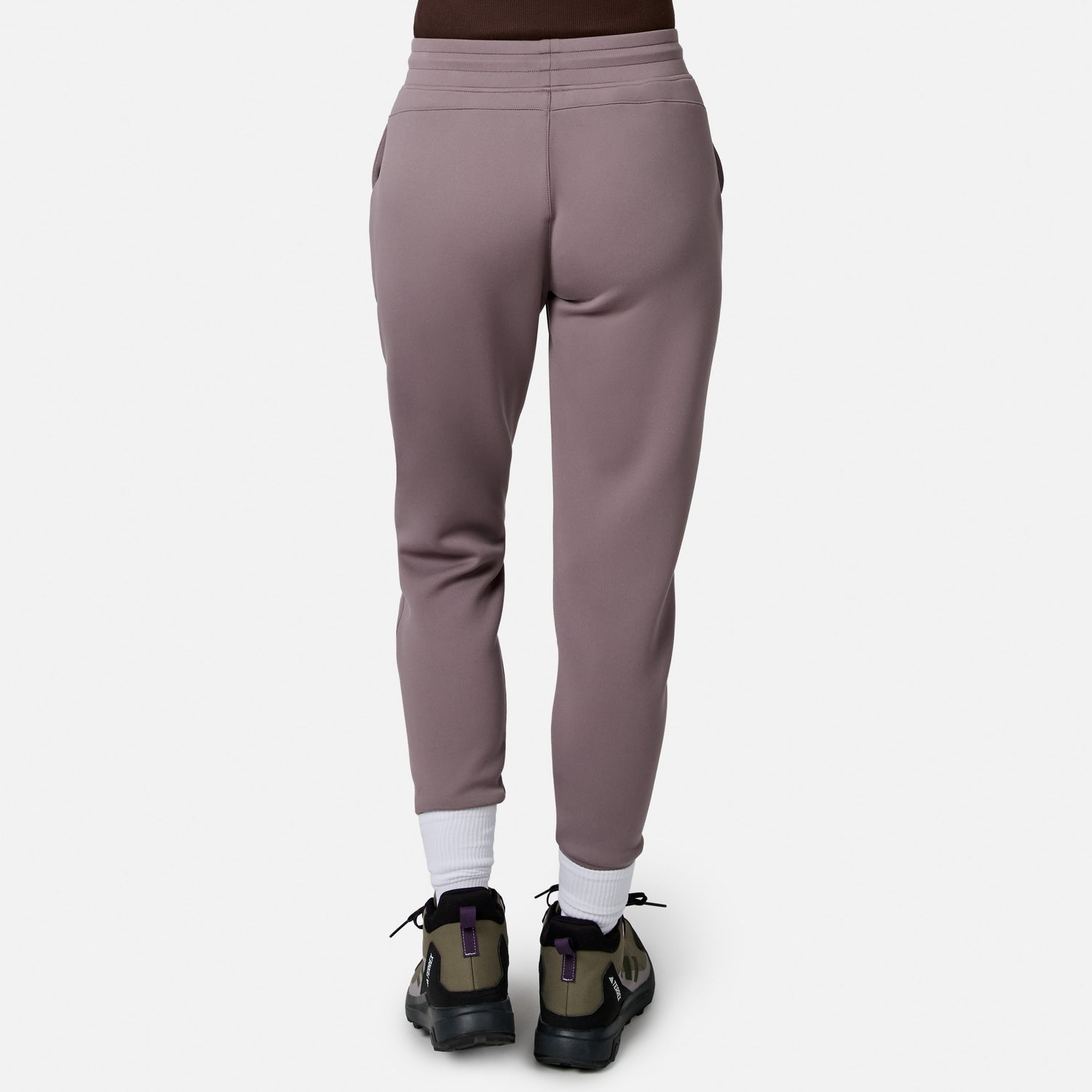 Person facing away, wearing Free Country Women’s Sueded Lush Jogger in mauve, white socks, and green-black sneakers with purple accents, standing against a plain white background.