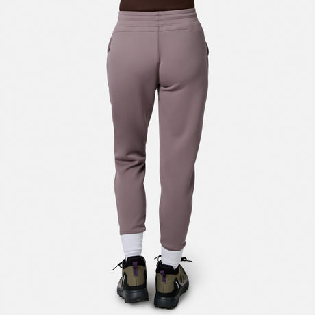 Person facing away, wearing Free Country Women’s Sueded Lush Jogger in mauve, white socks, and green-black sneakers with purple accents, standing against a plain white background.