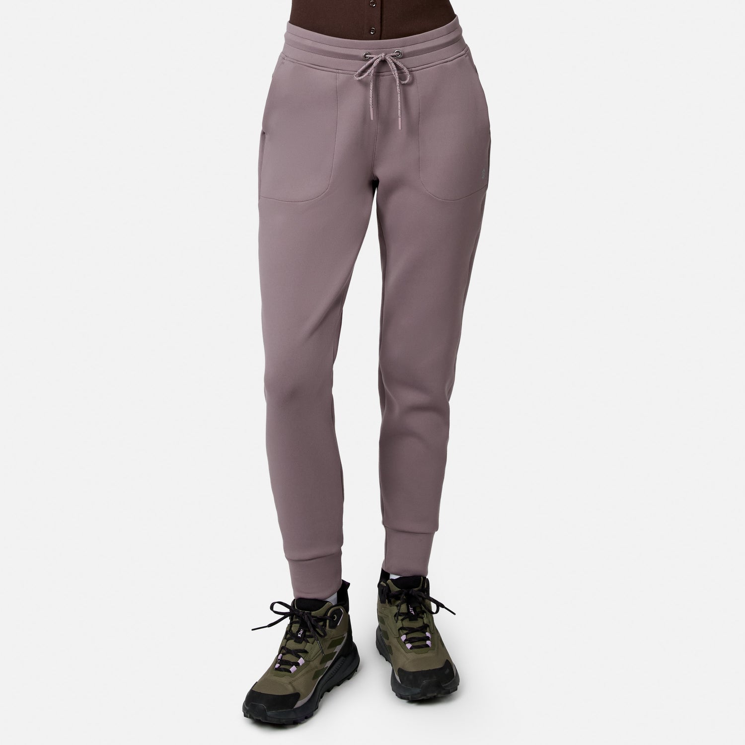 Model wears Free Country Women’s Sueded Lush Jogger in Zinc, featuring 4-way stretch, front pockets, and drawstring waist, paired with olive green and black hiking shoes. White background.