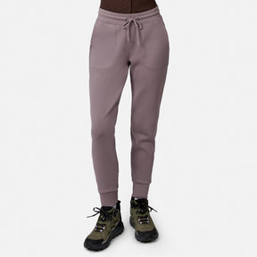 Model wears Free Country Women’s Sueded Lush Jogger in Zinc, featuring 4-way stretch, front pockets, and drawstring waist, paired with olive green and black hiking shoes. White background.