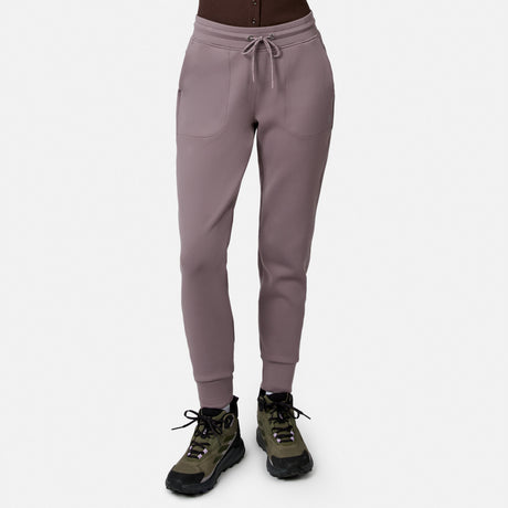 Model wears Free Country Women’s Sueded Lush Jogger in Zinc, featuring 4-way stretch, front pockets, and drawstring waist, paired with olive green and black hiking shoes. White background.