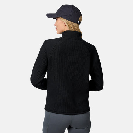 A person in a black Free Country Women’s Ripple Knit Half Zip Top, gray leggings, and a black baseball cap stands facing away from the camera against a plain white background.