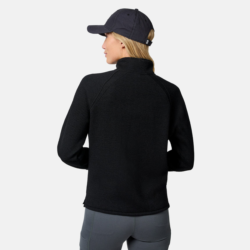 A person in a black Free Country Women’s Ripple Knit Half Zip Top, gray leggings, and a black baseball cap stands facing away from the camera against a plain white background.