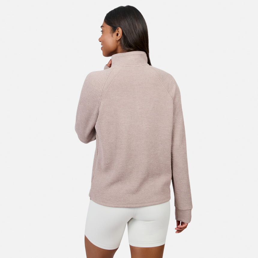 A woman with long dark hair faces away, wearing the Free Country Women’s Ripple Knit Half Zip Top in light pink and white shorts, styled casually against a plain white background.