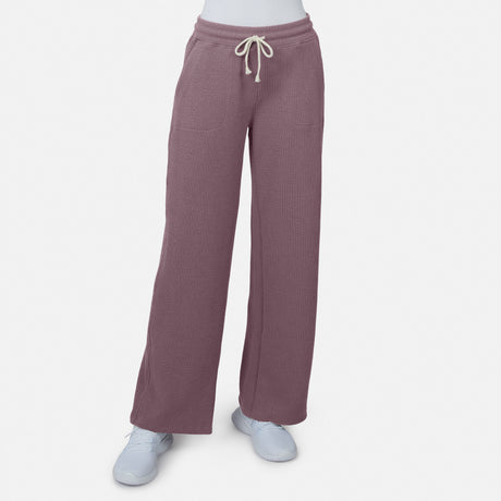 A woman wears Free Country’s Women’s Ripple Knit Long Wide Leg Pant in mauve with front pockets and a white drawstring, styled with white sneakers for relaxed comfort, standing against a plain white background.