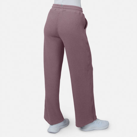 A person wears Free Country Women’s Ripple Knit Long Wide Leg Pants in maroon and white shoes, standing against a plain white background. The photo, taken from behind, showcases the pants’ relaxed fit and breathable ripple knit fabric.