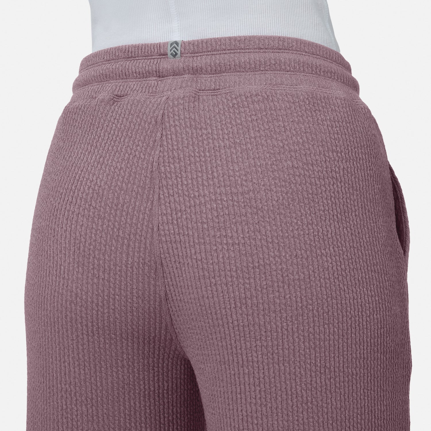 Close-up of a person wearing Free Country’s Women’s Ripple Knit Long Wide Leg Pant in mauve, paired with a white top. The image highlights the textured waistband and upper legs of these breathable pants against a plain background.