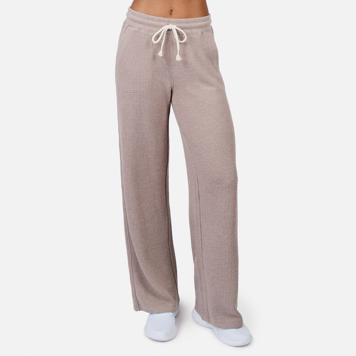 A person models the Free Country Women’s Ripple Knit Long Wide Leg Pant in taupe with a drawstring waist, paired with white socks and shoes, standing against a plain white background for a relaxed look.