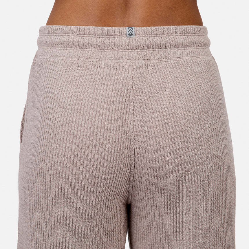 Close-up of the back of a person wearing Free Country Women’s Ripple Knit Long Wide Leg Pant in light brown, featuring ribbed fabric and a small gray and white logo centered at the waistband.
