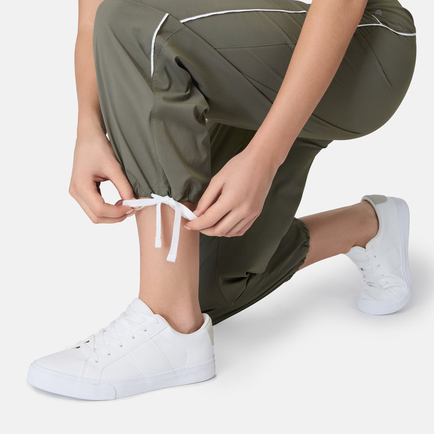 [Model is wearing size S] Person tying white sneakers with green pants on a light background