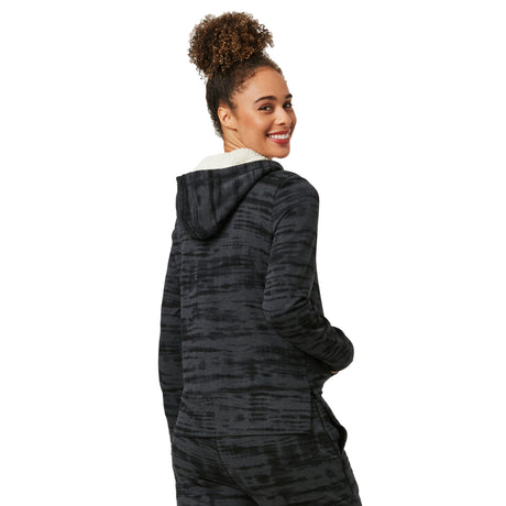 A smiling woman with curly hair in a high bun wears the Clearance Women's Luxe+ Sherpa Lined Jacket, a black and gray zip-up with ultra-comfy Sherpa lining, facing away but looking back over her shoulder.