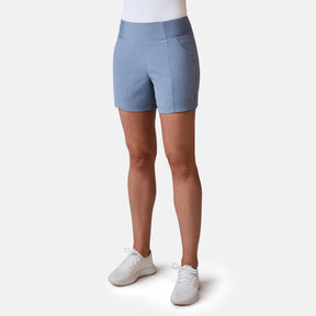 A person wearing Free Country’s Women’s Free 2 Explore Hybrid Short in light blue, featuring four-way stretch, side pockets, and a comfy waistband, pairs them with a white top and sneakers against a plain light background.