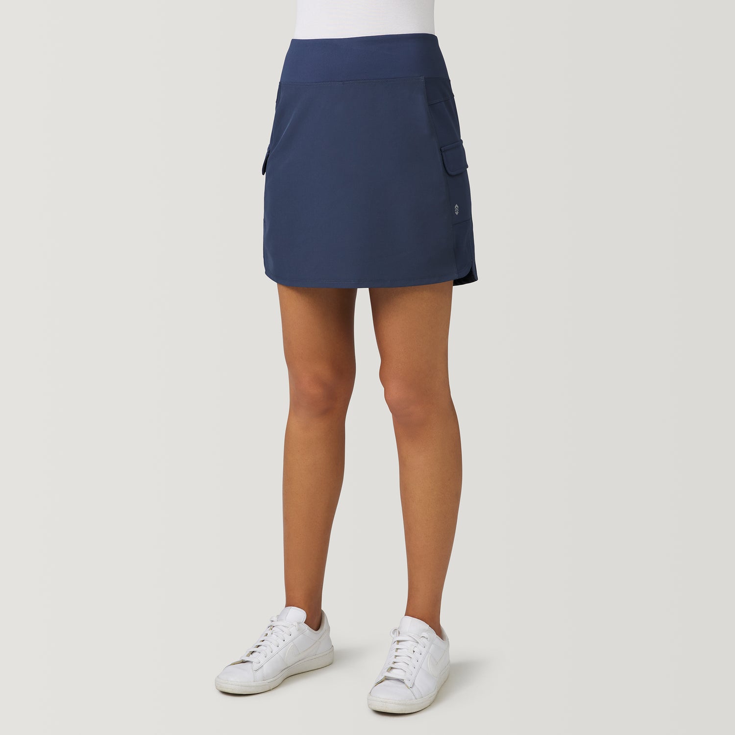 Navy blue moisture-wicking Women’s Free 2 Explore Hybrid Skort with side pockets, worn with a white shirt and white sneakers.