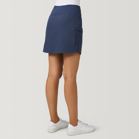 A person viewed from the back wearing a moisture-wicking dark blue Free Country Women’s Free 2 Explore Hybrid Skort with a side pocket and white sneakers.