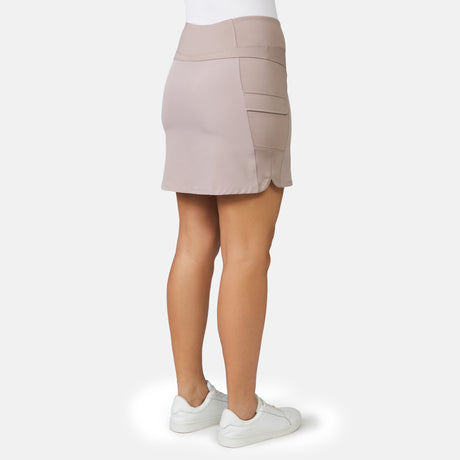 A person is seen from the back wearing Free Country’s Women's Free 2 Explore Hybrid Skort in light purple-beige with side pockets and four-way stretch fabric, paired with white sneakers and a white top against a plain light gray background.