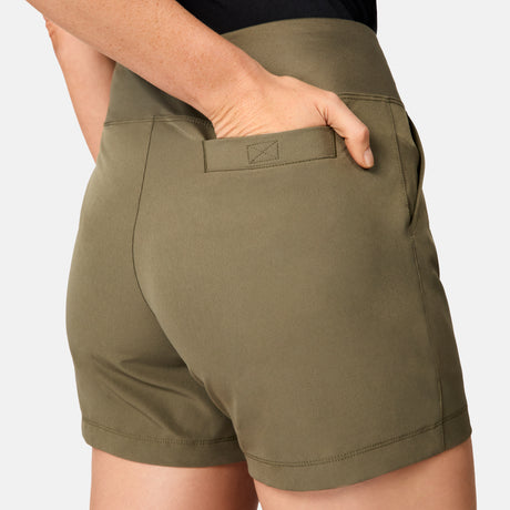 A woman wears the Free Country Women's Free 2 Explore Hybrid Short in olive green, posing waist-down with her right hand in the back pocket against a plain light background.