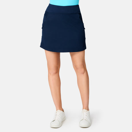 A person wears the Free Country Women's Free 2 Explore Hybrid Skort in blue, paired with a bright blue top and white sneakers. The image is cropped at the shoulders, focusing on the lower torso and legs against a plain white background.