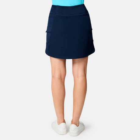 A person faces away in a Free Country Women's Free 2 Explore Hybrid Skort (navy, four-way stretch), paired with a light blue top and white sneakers, set against a plain white background.
