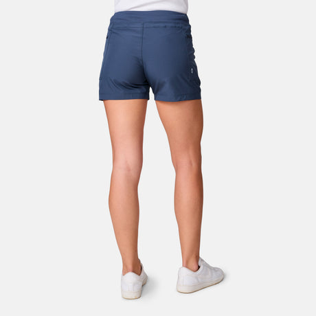 A woman is shown from the back wearing a white shirt, Free Country Women's Trail to Town Short in blue, and white sneakers against a plain white background.