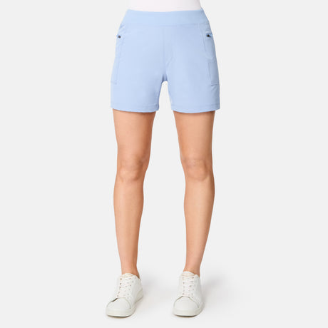 A woman wears Free Country Women's Trail to Town Shorts in light blue, paired with a white top and white sneakers, standing facing forward against a plain white background.