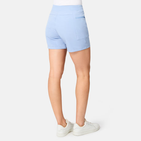 A person wearing Free Country Women's Trail to Town Short in light blue, a white top, and white sneakers stands with their back to the camera against a plain white background.