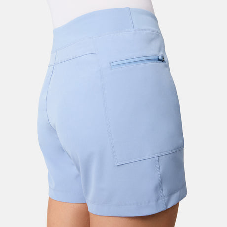 A close-up of a person wearing Free Country Women's Trail to Town Short in light blue, featuring stretch knit fabric, a back cargo zipper pocket, and a side pocket, set against a plain white background.