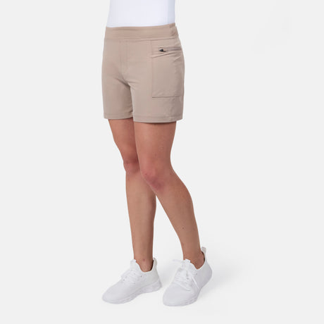 A person wearing Free Country Women's Trail to Town Short in light beige with a small front pocket and white sneakers, standing against a plain white background. Upper body is not visible.