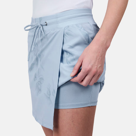 Someone wears the Free Country Women's Trail to Town Skort in light blue, showing the subtle floral pattern and built-in four-way stretch shorts for comfort during any activity.