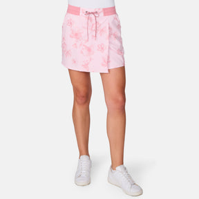 A person wears the Free Country Women's Trail to Town Skort in light pink floral with a drawstring waist and four-way stretch, paired with white sneakers. The background is plain white.