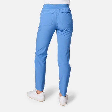 A person faces away, wearing Free Country Women's Get Out There Ruch Up Pant in light blue (UPF 50+, back pockets) with white sneakers, against a plain white background.
