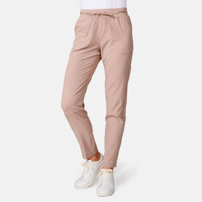 A person models the Women's Get Out There Ruch Up Pant by Free Country—light pink jogger-style with front pockets and a drawstring waist—paired with white sneakers, against a plain white background.