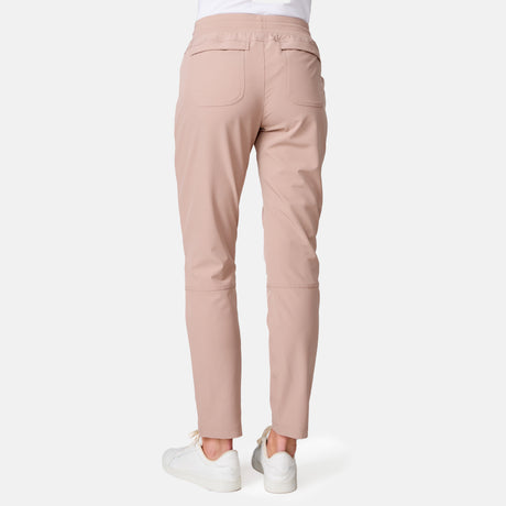 A person is shown from the back, wearing Free Country Women's Get Out There Ruch Up Pant in light pink with two back pockets and a relaxed fit, paired with white sneakers against a plain white background.
