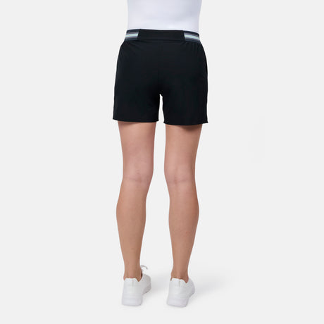 A woman, seen from the back against a plain white background, is wearing a white top, Free Country Women's Explorer Short with a striped waistband, and white sneakers.