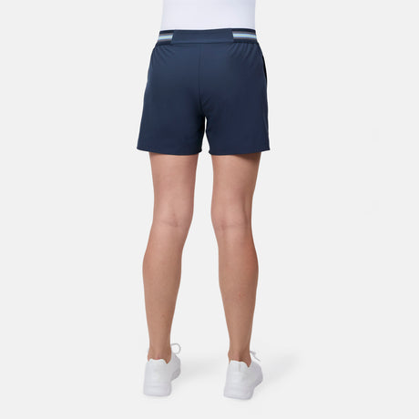 A woman is shown from the back wearing Free Country Women's Explorer Short in navy blue, a white top, and white sneakers, standing against a plain white background.