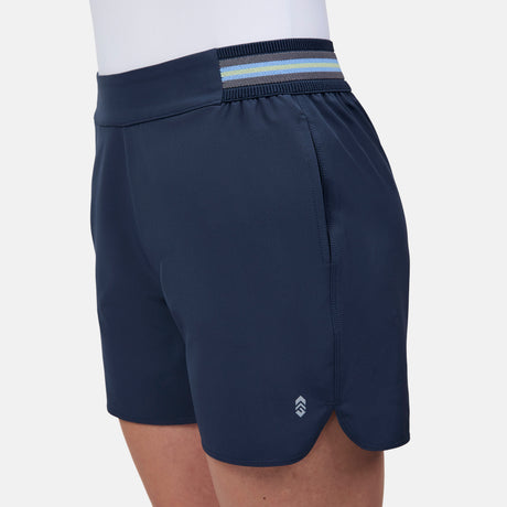 A person wears Free Country Women's Explorer Short in navy blue, featuring a small white logo near the hem, a striped blue elastic waistband, and moisture-wicking fabric for all-day comfort.