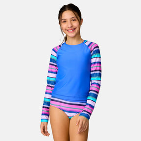 A smiling girl wears the Girls' Marina Stripe Rash Guard and Bikini Swim Set by Clearance—a blue long-sleeve rash guard with colorful striped sleeves and matching bottoms—standing against a plain light background.