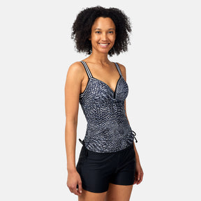 A woman with curly hair smiles while wearing the Women's Sea Skin Track Stripe Tankini by Clearance, featuring wireless molded cups and adjustable straps, paired with black swim shorts, against a plain light background.