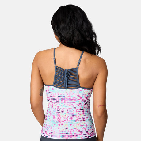 A woman with long dark hair wears the Women's Mirage High Neck Macrame Back Tankini Top by Clearance in a pink, blue, and white abstract print with ladder-back straps and UPF 50+ fabric, facing away against a light background.