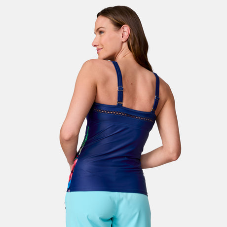 A woman with long brown hair is shown from the back wearing the Clearance Women's Seashore Blossom High Neck Tankini Top in navy blue, paired with turquoise quick-dry swim shorts, as she smiles over her shoulder against a plain light background.